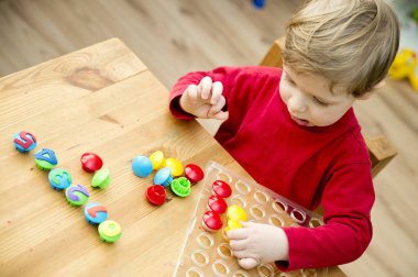 Oyun sayıyorum. Belirtilen numaraya göre doğru sayıda kapak al. Küçük çocuk görevini yerine getirdi. Erken eğitim. Oyuncak hayal gücünü, yaratıcılığı, el-göz koordinasyonunu canlandırır..