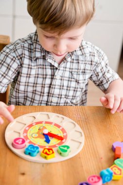 Çocuk tahta saat numaralarıyla oynuyor. Farklı delikle eşleşen farklı numara. Tahta numara bulmacası. Çocukların iyi motor becerileri geliştirmesi için uygulama, oyun yoluyla mantıklı düşünme. 