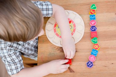 Çocuk tahta saat numaralarıyla oynuyor. Farklı delikle eşleşen farklı numara. Tahta numara bulmacası. Çocukların iyi motor becerileri geliştirmesi için uygulama, oyun yoluyla mantıklı düşünme. 