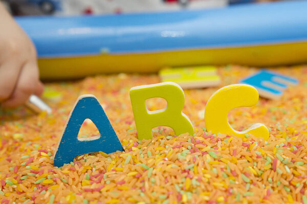 Ребенок изучает азбуку. Раннее образование для детей с цветным рисом в качестве сенсорных элементов. Терапия для детей с легким обучением.