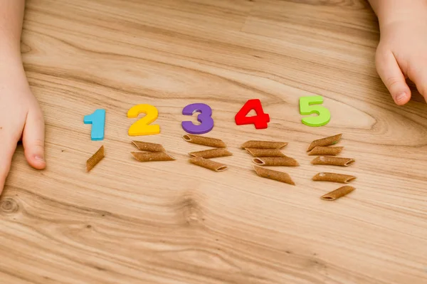 Math with fun. Counting uncooked pasta and marking with colored natural wood numbers.