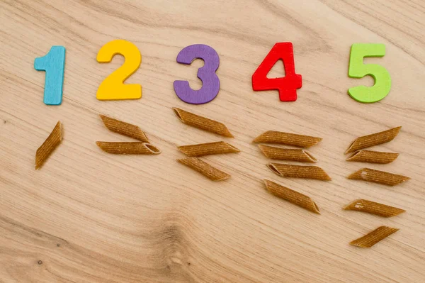 Math with fun. Counting uncooked pasta and marking with colored natural wood numbers.