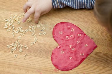 Sevgililer Günü teması, sayılar, harfler ve sembollerle dolu oyun hamurundan yapılmış kalp okuması. iyi motor becerileri, erken eğitim. Annelerin evde çocuk beyin aktivitesi yapma fikri