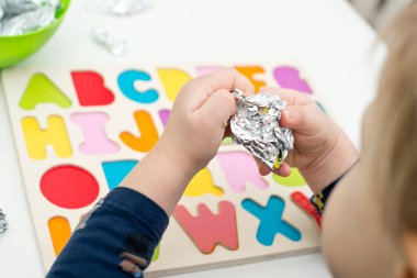 Tahta alfabe harfleriyle oynayan iki yaşında bir çocuk. Folyoya sarılı mektuplar. Entellektüel oyun, erken eğitim için anaokulu uygulaması. Sözlü ve bellek alıştırması.