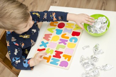 Tahta alfabe harfleriyle oynayan iki yaşında bir çocuk. Folyoya sarılı mektuplar. Entellektüel oyun, erken eğitim için anaokulu uygulaması. Sözlü ve bellek alıştırması.