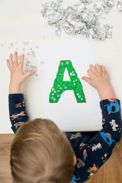 Two year boy decorating play dough letter \