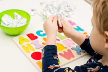 Tahta alfabe harfleriyle oynayan iki yaşında bir çocuk. Folyoya sarılı mektuplar. Entellektüel oyun, erken eğitim için anaokulu uygulaması. Sözlü ve bellek alıştırması.