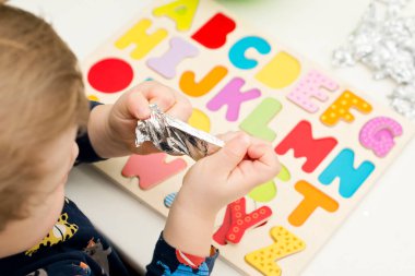 Tahta alfabe harfleriyle oynayan iki yaşında bir çocuk. Folyoya sarılı mektuplar. Entellektüel oyun, erken eğitim için anaokulu uygulaması. Sözlü ve bellek alıştırması.
