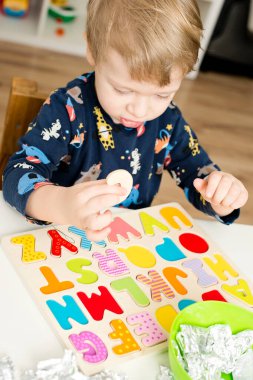 Tahta alfabe harfleriyle oynayan iki yaşında bir çocuk. Folyoya sarılı mektuplar. Entellektüel oyun, erken eğitim için anaokulu uygulaması. Sözlü ve bellek alıştırması.