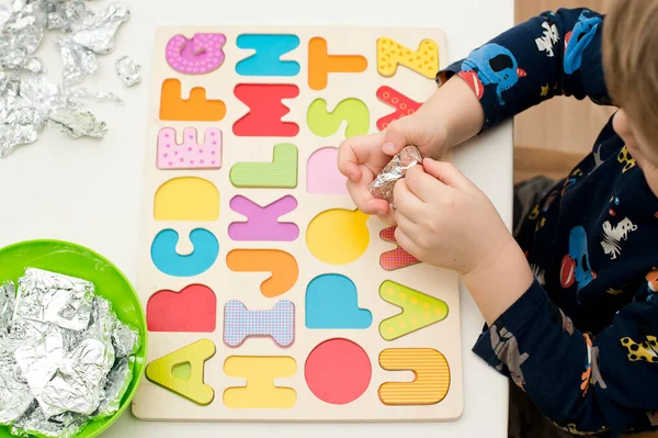 Two year boy playing with wooden alphabet letters board. Letters wrapped in foil. Intellectual game, preschool implement for early education. Verbal and memory training exercise.