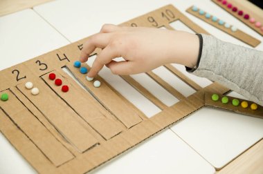 Pamuk yumaklarıyla kayışları numaralandırılmış oyuğa yerleştirin. Anaokulları için okul öncesi eğitim yardımı. Çocuklar erken yaşta zeka için montessori setini öğreniyorlar.