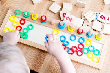 Çocuk farklı renkte ahşap halkalarla oynuyor. Sıralama, iyi motor beceriler, eğitim ve beyin egzersizi için terapi görevi. Matematik oyunu da dahil. Montessori tipi uygulama. Tahta oyuncaklar.