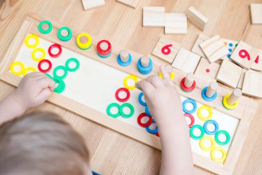 Çocuk farklı renkte ahşap halkalarla oynuyor. Sıralama, iyi motor beceriler, eğitim ve beyin egzersizi için terapi görevi. Matematik oyunu da dahil. Montessori tipi uygulama. Tahta oyuncaklar.