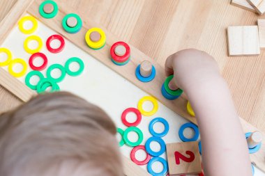 Çocuk farklı renkte ahşap halkalarla oynuyor. Sıralama, iyi motor beceriler, eğitim ve beyin egzersizi için terapi görevi. Matematik oyunu da dahil. Montessori tipi uygulama. Tahta oyuncaklar.