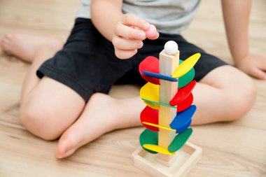 Tahta mermer yarış kulesi. Çocuklar oyun oynamak için oyun oynarlar. Çocuk topu başlangıç pozisyonuna getiriyor. Evdeki etkinlikler. Tablo ve zemin oyunu.