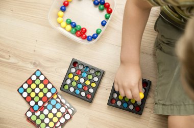Childs 'ın elleri renkli ahşap misketlerin üzerinde. Renkli mantık oyunu. Anaokulu ve ilkokul için bir araç. Montessori, beyin egzersizi. Odaklanma, sabır ve dikkat alıştırması..
