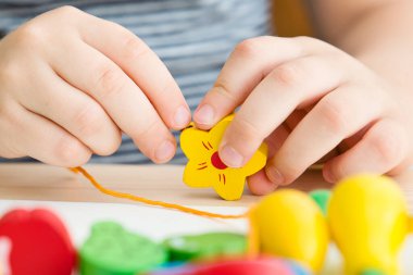 İnce motorlu yetenekler. Bebekler ve yeni yürümeye başlayanlar için boncuk dizme oyuncakları. Çocuklar için İplik Etkinliği. Çocuk yerde oturup ahşap ağaç ve bahçe eşyalarıyla oynuyor..