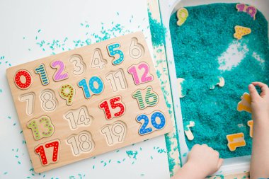 Çocuk oyun yoluyla numaraları öğreniyor. Renkli pirinç ve ahşap sayılarda duyusal aktivite. Evde eğitim, okul öncesi eğitim, Montessori metodu