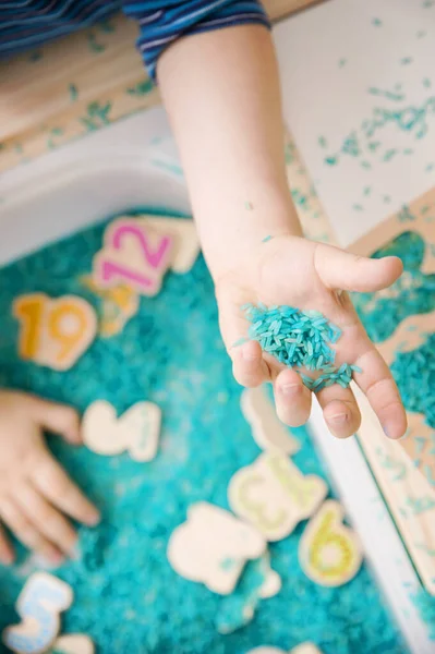 Çocuk oyun yoluyla numaraları öğreniyor. Renkli pirinç ve ahşap sayılarda duyusal aktivite. Evde eğitim, okul öncesi eğitim, Montessori metodu