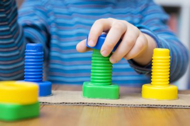 Şekiller, renkler ve ince motor beceriler. Yeni yürümeye başlayan çocuk cıvatanın fındığını çeviriyor. Eşleşen iplikte doğru renk bölümünü bükme görevi. çocuk mimikçi, konsantre, sürece dahil..