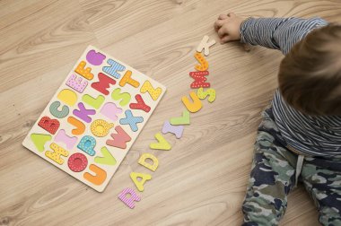 Yerde tahta harflerle oynayan iki yaşında bir çocuk var. Entellektüel oyun, erken eğitim için anaokulu uygulaması. Sözlü ve bellek alıştırması.