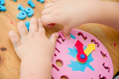 Saat oyuncağıyla zaman geçiren küçük bir çocuk, saati söylemeyi öğrenen bir çocuk, yeni yürümeye başlayan çocuklar için oynayarak öğrenme kavramı..
