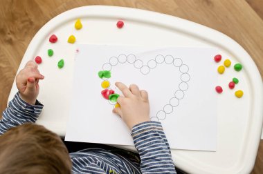 Annem için sevgililer günü tebrik kartı hazırlıyorum. Küçük çocuk baskılı kağıt kalbe hamur uyguluyor. Güzel motor beceriler, parmak koordinasyonu. bebekler için erken eğitim