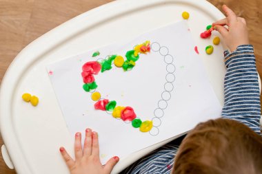 Annem için sevgililer günü tebrik kartı hazırlıyorum. Küçük çocuk baskılı kağıt kalbe hamur uyguluyor. Güzel motor beceriler, parmak koordinasyonu. bebekler için erken eğitim