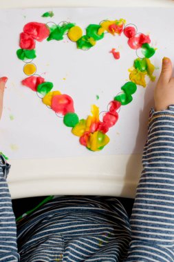 Annem için sevgililer günü tebrik kartı hazırlıyorum. Küçük çocuk baskılı kağıt kalbe hamur uyguluyor. Güzel motor beceriler, parmak koordinasyonu. bebekler için erken eğitim