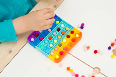Çocuk duyusal oyuncak Pop-it ile oynuyor. Kaliteli motor becerileri için araç, saymaya başlamak için araç, birincil aritmetik işlemlerini öğrenmek. Parmak uyumu ve rahatlama için bir yatıştırıcı..