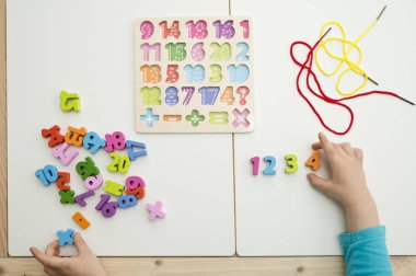 Çocuk oyun yoluyla numaraları öğreniyor. Tahta sayılar ve ayakkabı bağcıklarıyla duyusal aktivite. Evde eğitim, okul öncesi eğitim, Montessori metodolojisi. sayılar dizisi, aritmetik problemler.
