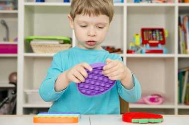 Çocuk duyusal oyuncak Pop-it ile oynuyor. Kaliteli motor becerileri için araç, saymaya başlamak için araç, birincil aritmetik işlemlerini öğrenmek. Parmak uyumu ve rahatlama için bir yatıştırıcı..