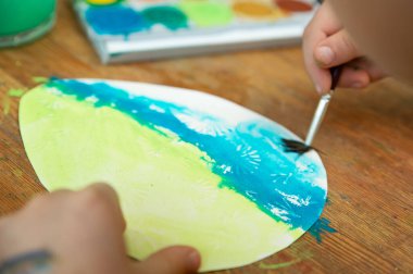 Paskalya yumurtası boyayan bir çocuk. Evde yaratıcı aktivite. Boya ve kağıt kullanarak..