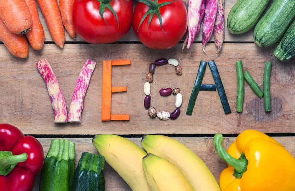 Palabra vegana sobre fondo de madera y verdura — Foto de Stock