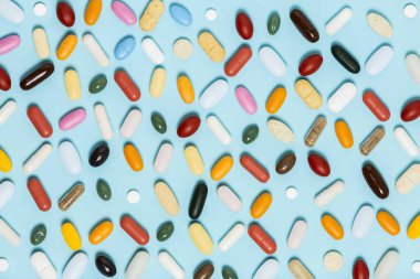 Parlak açık mavi arka planda ilaç hapları, haplar ve kapsüllerle yapılan modaya uygun bir model. Tıbbın yaratıcı kavramları. Renkli kâğıt arkaplanı olan en düşük tarz. Moda renkleri