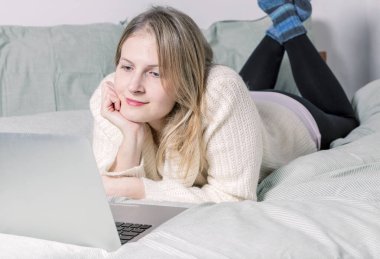 Dizüstü bilgisayarının önünde bacakları hafifçe kaldırılmış bir kadın yatakta yatıyordu. Karantina karantinasında evden çalışıyor. Sosyal Mesafe Öz İzolasyonu.