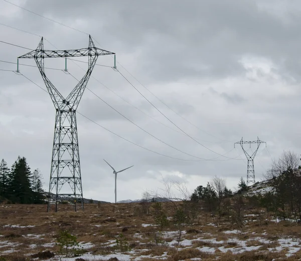 Windmill farm next to power lines during wintertime in Norway. Clean energy concept
