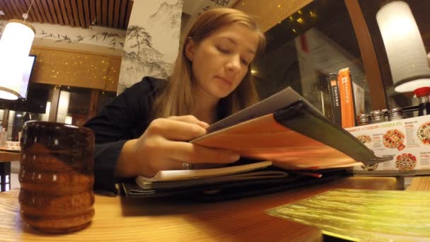 La chica está estudiando en el menú restaurante japonés — Vídeo de stock