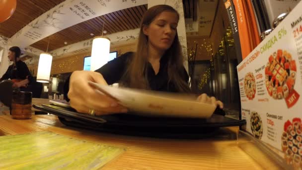 La chica está estudiando en el menú restaurante japonés — Vídeos de Stock