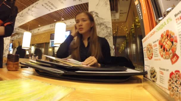 Das Mädchen studiert im japanischen Restaurant auf der Speisekarte — Stockvideo