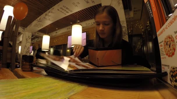 La chica está estudiando en el menú restaurante japonés — Vídeo de stock