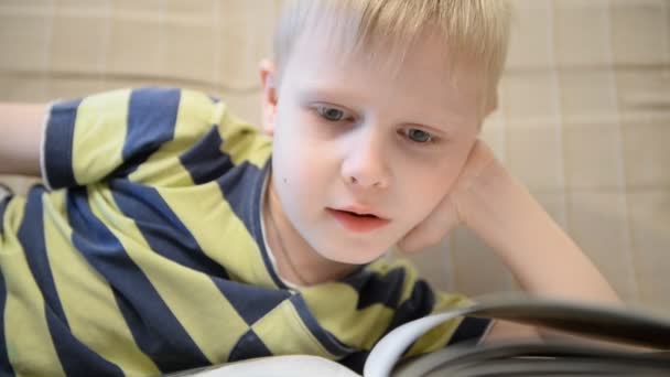 Pojke 5 år läser en bok hemma på soffan — Stockvideo