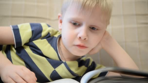 Niño 5 años leyendo un libro en casa en el sofá — Vídeos de Stock