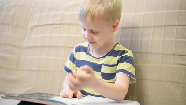 Мальчик 5 лет читает книгу дома на диване — стоковое видео