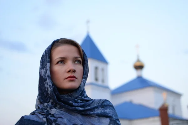 En flicka av slaviska ryska utseende i en halsduk på bakgrund av kyrkan — Stockfoto