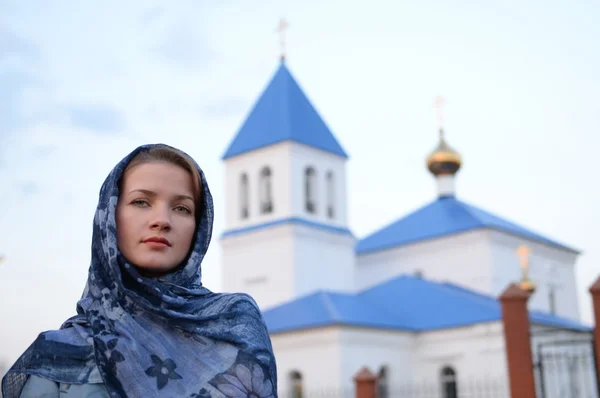 En flicka av slaviska ryska utseende i en halsduk på bakgrund av kyrkan — Stockfoto