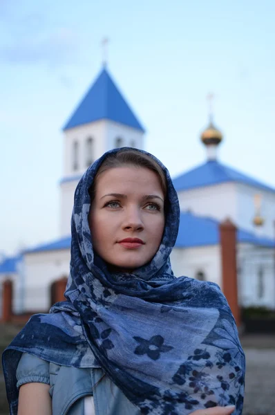En flicka av slaviska ryska utseende i en halsduk på bakgrund av kyrkan — Stockfoto