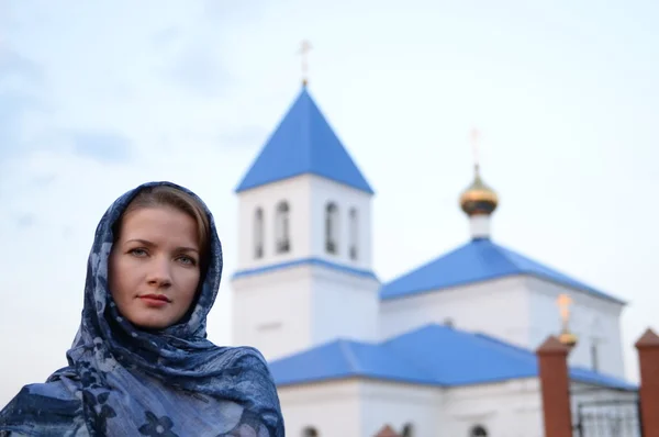 En flicka av slaviska ryska utseende i en halsduk på bakgrund av kyrkan — Stockfoto