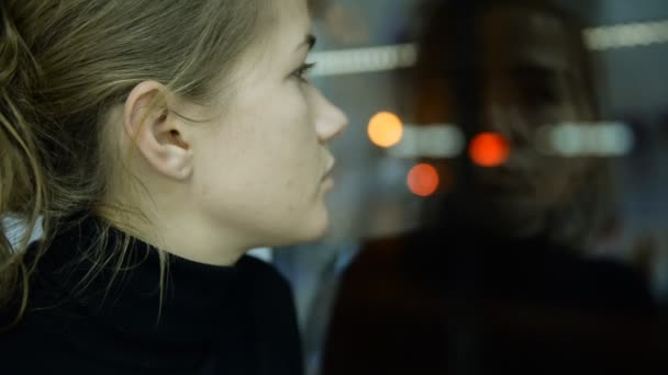 Город, витрина. Депрессивная женщина на фоне вечерней улицы, автомобилей и огней — стоковое видео