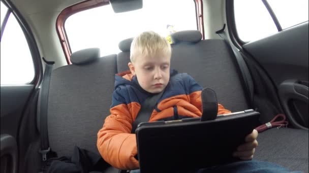 A criança pré-escolar (menino) com computador tablet viaja no banco de trás do carro — Vídeo de Stock